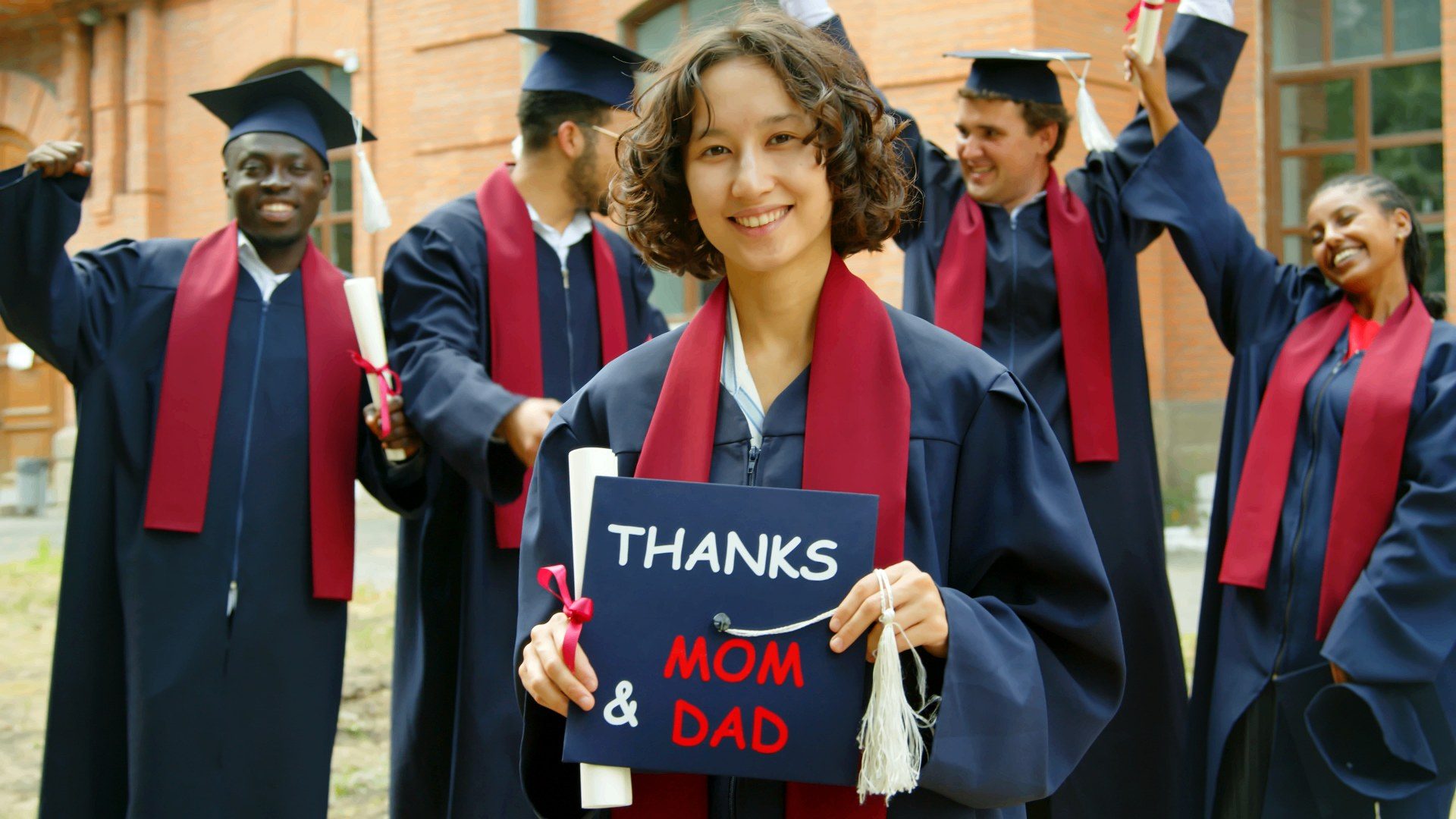 A graduate smiling with a 'Thanks Mom & Dad' cap.